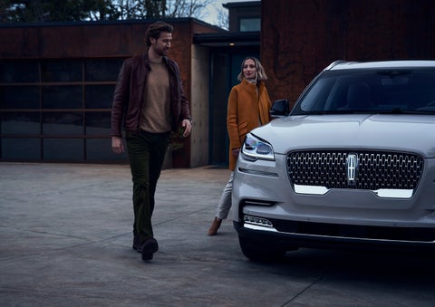 A man and a woman approaching a 2024 Lincoln Aviator® SUV, which illuminates certain lights when they are close | Rogers Lincoln in Midland TX