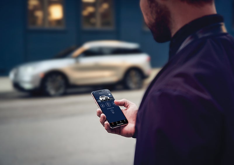 A person is shown interacting with a smartphone to connect to a Lincoln vehicle across the street. | Rogers Lincoln in Midland TX