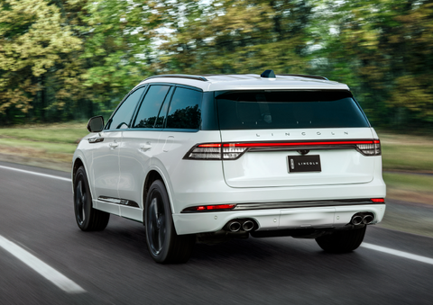 A white 2025 Lincoln Aviator® SUV is being driven away down a road lined with colorful trees. | Rogers Lincoln in Midland TX