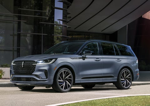 A gray 2025 Lincoln Aviator® SUV is parked outside a modern building showcasing the driver’s side of the vehicle. | Rogers Lincoln in Midland TX