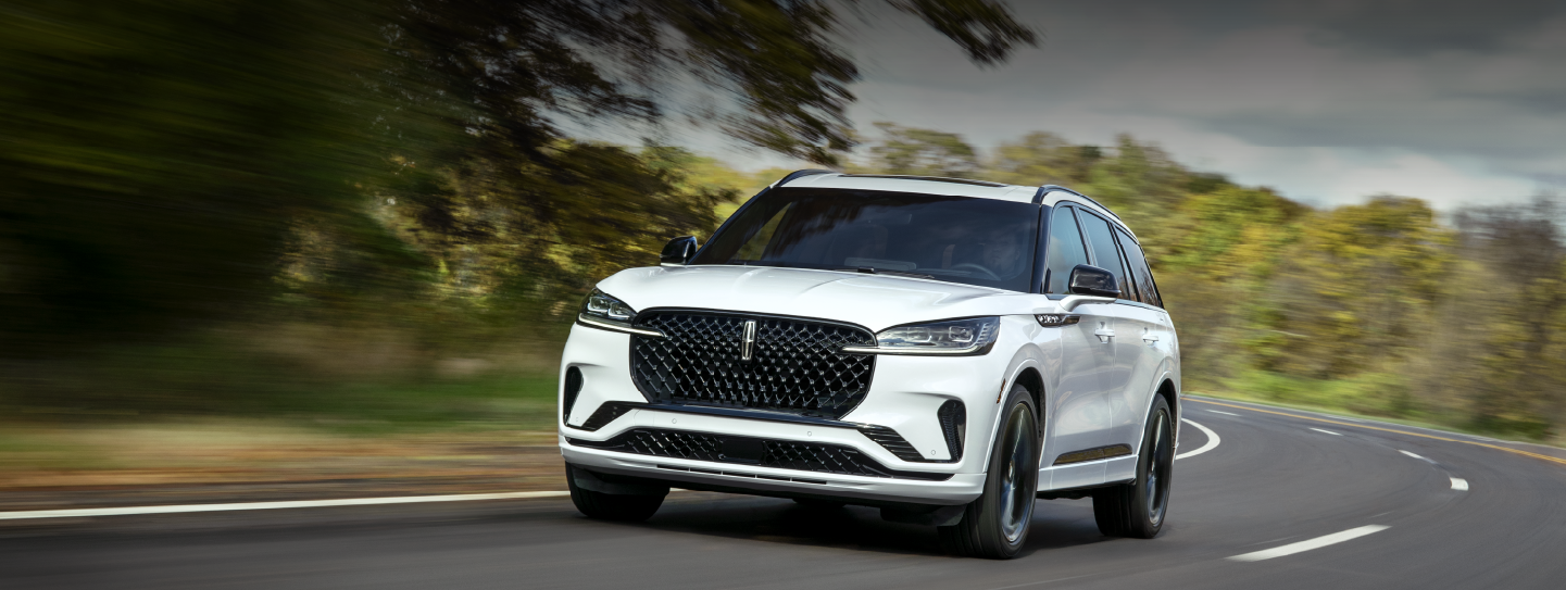 A white 2025 Lincoln Aviator® SUV is being driven down a road lined with trees. | Rogers Lincoln in Midland TX