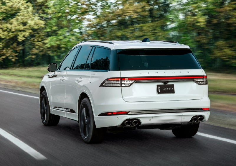 A white 2026 Lincoln Aviator® SUV is being driven away down a road lined with colorful trees. | Rogers Lincoln in Midland TX