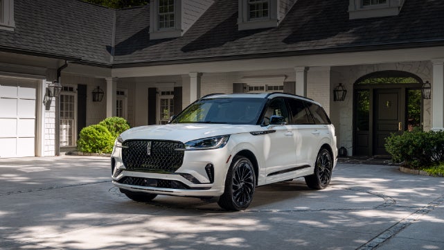 A white 2026 Lincoln Aviator® SUV is parked in the driveway of a luxury home. | Rogers Lincoln in Midland TX