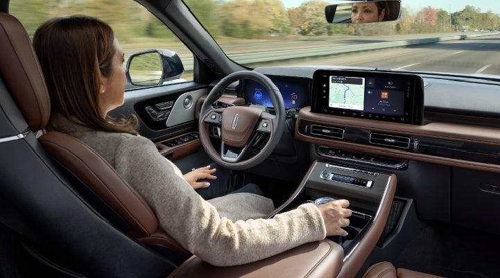 A 2027 Lincoln Aviator® SUV is being driven hands-free on a highway lined with trees. | Rogers Lincoln in Midland TX