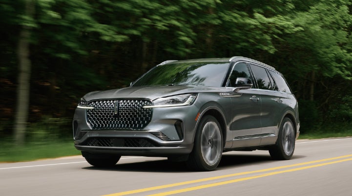 A 2027 Lincoln Aviator® SUV is being driven down a road lined with trees. | Rogers Lincoln in Midland TX